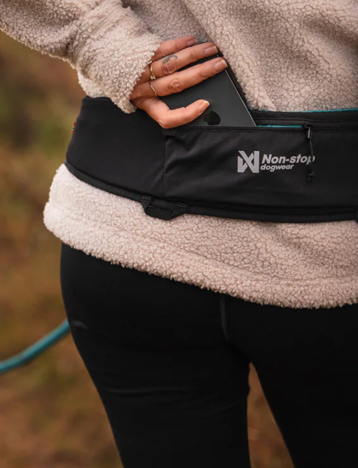 Person wearing a black waist bag with 'Non-stop Dogwear' logo, holding a phone.