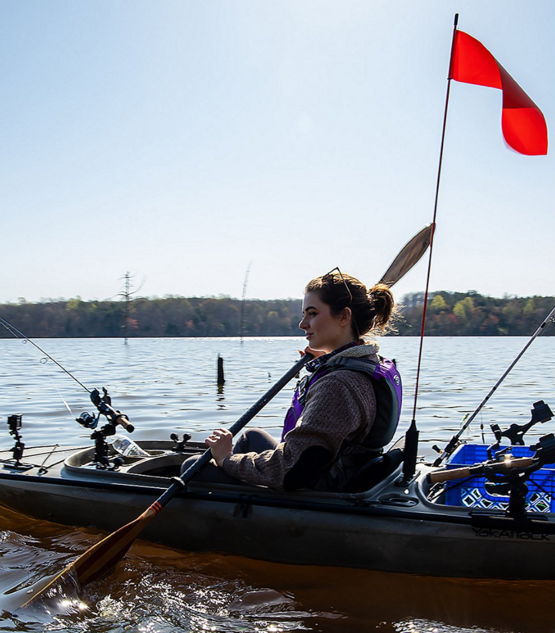 Person in a kayak on water with fishing gear and a red flag