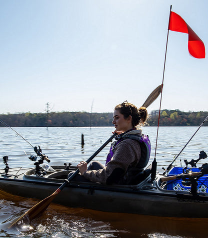 Person in a kayak on water with fishing gear and a red flag